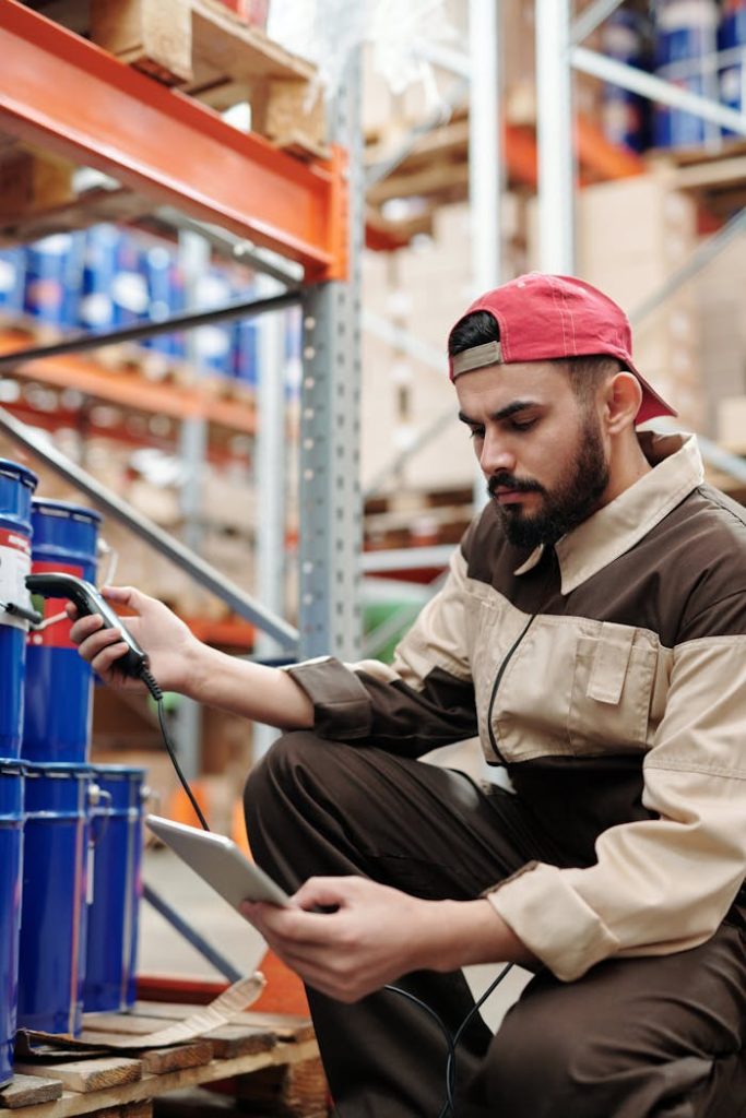 Man in warehouse scanning items with digital tablet, focused on inventory management.